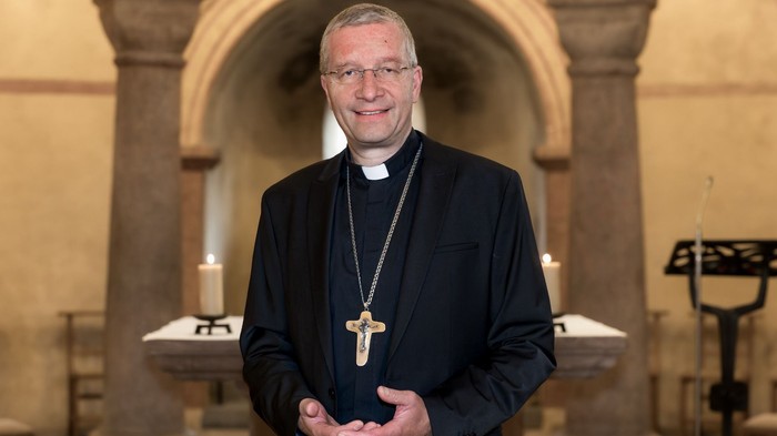Ein Mann in schwarzer Priesterkleidung vor einem Altar.