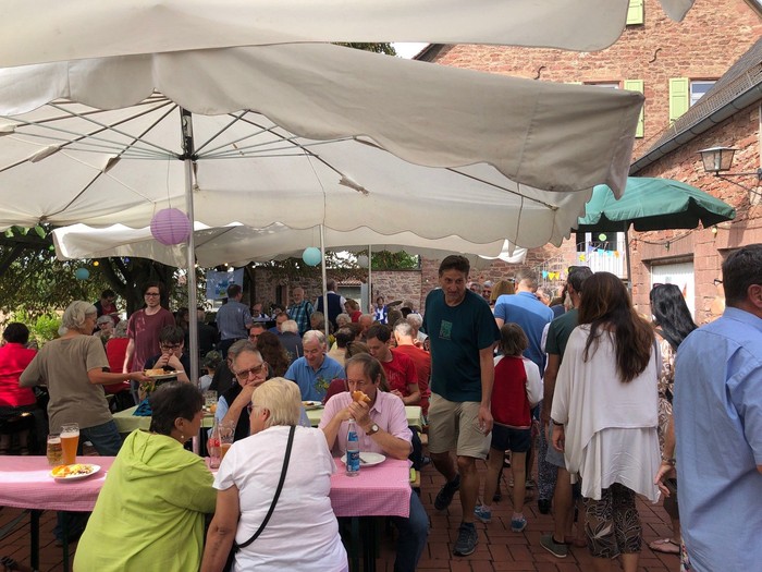 Draußen stattfindende gesellige Zusammenkunft mit Menschen, die Essen, Getränke und Gespräche unter großen Sonnenschirmen genießen.