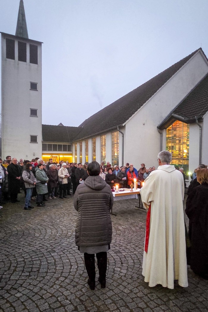 Eine Menschenmenge bei trüben Wetter vor einer hell erleuchteten Kirche.