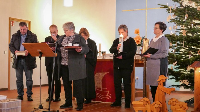 Mehrere Menschen halten verschiedene Gegenstände vor einem Altar.