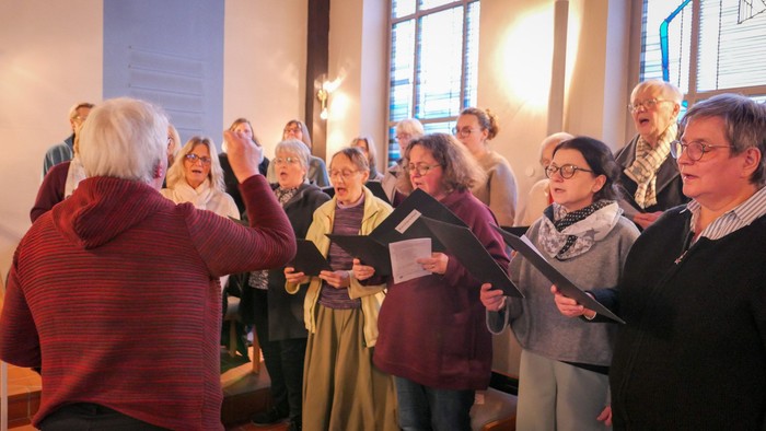 Ein Frauenchor singt in einer Kirche, gesehen über die Schulter der Dirigentin.