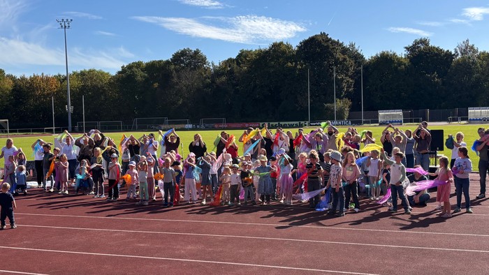 Auf der Laufbahn des Jahnstadions Bottrop stehen viele Kinder vor einem Altar und schwenken bunte Tücher. Sie tanzen zu einem Lied. In der Mitte Pfarrerin Annika Wilinski