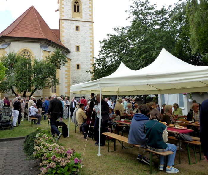 Gemeinschaftliches Treffen im Freien mit Menschen, die unter Zelten in der Nähe einer historischen Kirche sitzen.