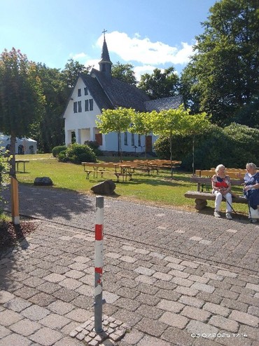 Personen auf einer Bank - Kapelle im Hintergrund