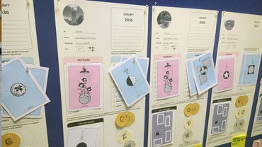 An einer Stellwand hängen die Steckbriefe der Gebäude mit den zugeordeneten Strategien sowie symbolische Münzen für den Ressourcenbedarf. An einer Stellwand hängen die Steckbriefe der Gebäude mit den zugeordeneten Strategien sowie symbolische Münzen für den Ressourcenbedarf.