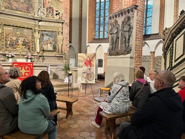 Menschen sitzen um das Bild im Altarraum herum