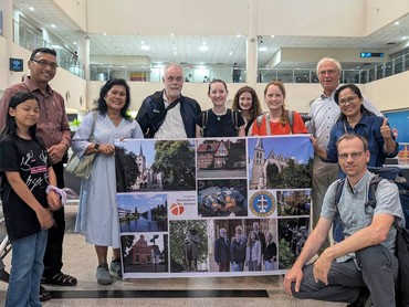 Gruppe, die mit einer Collage aus Reisefotos aus einer europäischen Stadt posiert und in einer Flughafenumgebung lächelt.