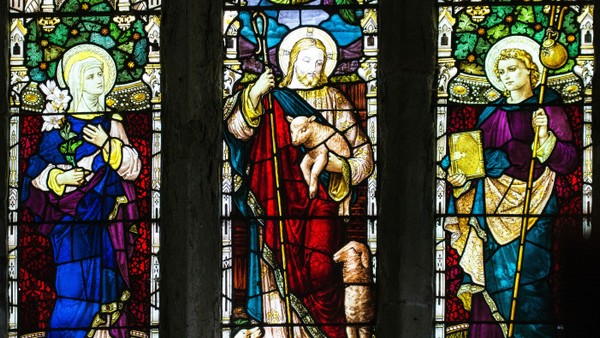 Buntglasfenster mit drei religiösen Figuren, die Gegenstände halten.