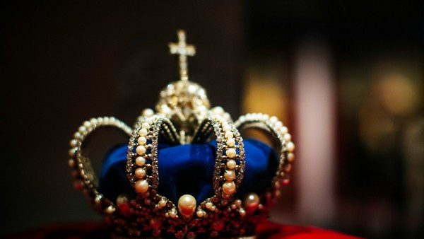 Eine Krone mit einem großen blauen Edelstein und kleineren Juwelen, gekrönt von einem Kreuz.