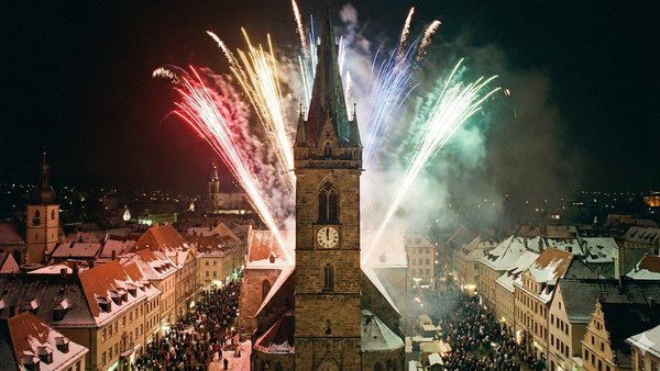 Lebhafte Feuerwerke erleuchten einen historischen europäischen Stadtplatz, der nachts mit Zuschauern gefüllt ist.